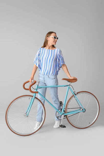 Pretty teenage girl in sunglasses with bicycle on light background - Zdjęcie, obraz