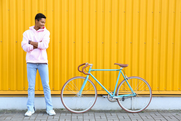 Adolescente afroamericano con bicicleta cerca de la valla amarilla - Foto, Imagen