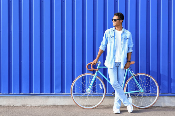 Adolescent afro-américain en lunettes de soleil avec vélo près de la barrière bleue - Photo, image
