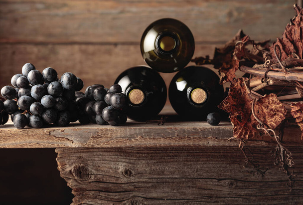 Butelki czerwonego wina z winogronami i suszoną winoroślą na starym drewnianym stole. Przestrzeń kopiowania. - Zdjęcie, obraz