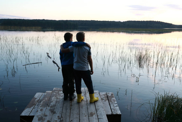 Children standing on wooden bridge by lake at sunset, Karelia - Foto, imagen