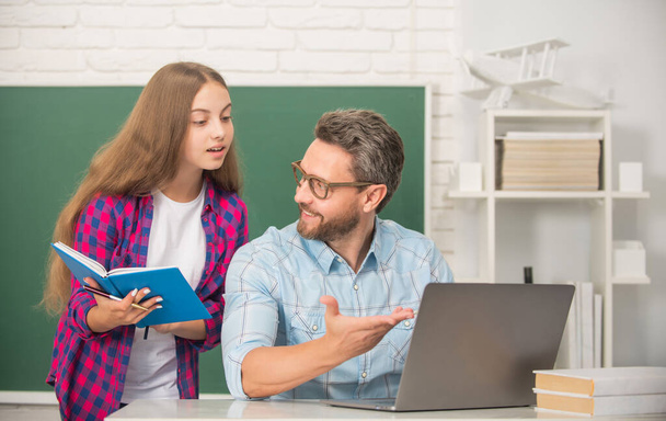 περίεργος έφηβος κορίτσι και ο δάσκαλος άνθρωπος στο γυμνάσιο με βιβλίο εργασίας και υπολογιστή στον πίνακα, πατρότητα - Φωτογραφία, εικόνα