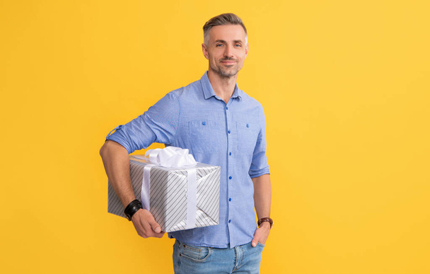 χαμογελαστός άνθρωπος κρατήστε το παρόν κουτί σε κίτρινο φόντο, ψώνια - Φωτογραφία, εικόνα