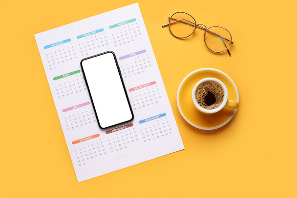 Paper calendar for 2022 year, mobile phone, eyeglasses and cup of coffee on color background - Zdjęcie, obraz