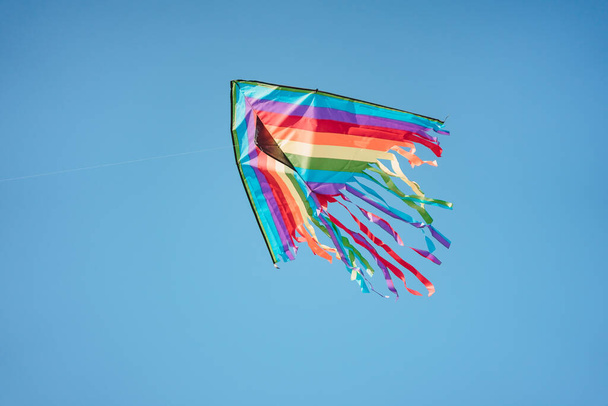 A colored kite is flying in the blue sky. A plane made of fabric with ribbons, made with his own hands, hovers in the air alone - Zdjęcie, obraz