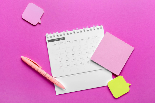 Flip Paper Kalender für April 2022, leere Haftnotizen und Stift auf farbigem Hintergrund - Foto, Bild