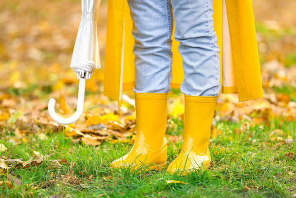 Nainen, jolla on sateenvarjo yllään keltainen sadetakki ja purukumit syksyllä puistossa - Valokuva, kuva