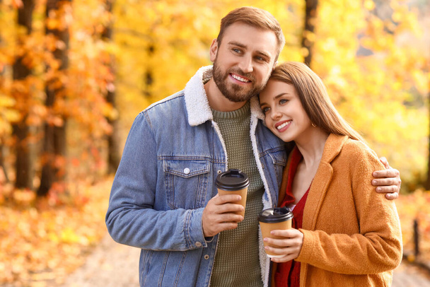 Young beautiful couple holding paper cups with drink in autumn park - Photo, Image