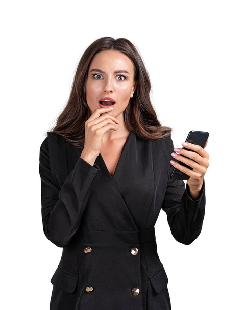 Young attractive shocked businesswoman wearing formal suit is holding smartphone. Concept of contemporary successful business people. Isolated over white background - Photo, Image