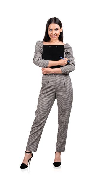 Young attractive businesswoman wearing formal jumpsuit is holding clipboard. Concept of contemporary successful business people. Isolated over white background - Foto, immagini