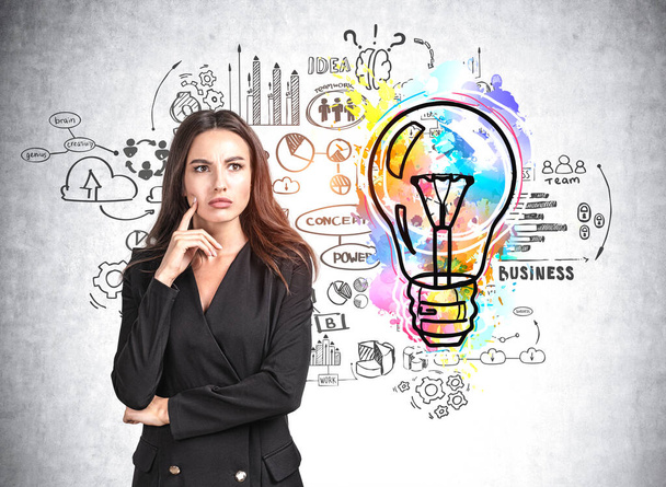Office woman in black suit think, finger to face, big lightbulb with circuit of business plan drawing, graphs and financial analysis. Concept of brainstorm and startup - Foto, Imagen