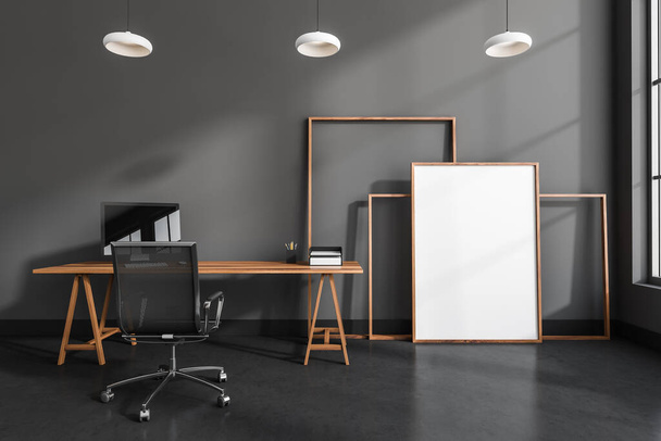 Black office room interior with armchair and computer on wooden table, window. Mockup blank canvas frame on dark concrete floor, 3D rendering - 写真・画像