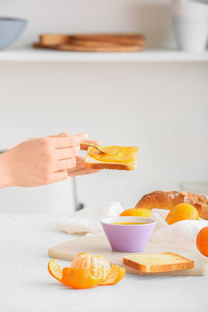 Woman spreading tasty tangerine jam onto toast at table in kitchen - 写真・画像