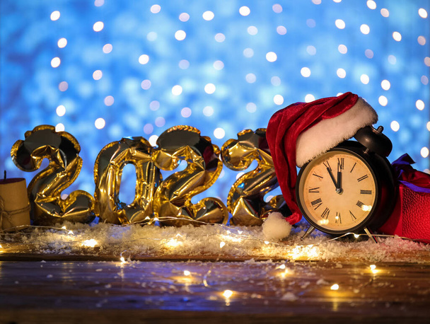 Різдвяний годинник з капелюхом Санта, сніг і фігура 2022 року з повітряних куль на столі на розмитому фоні
 - Фото, зображення