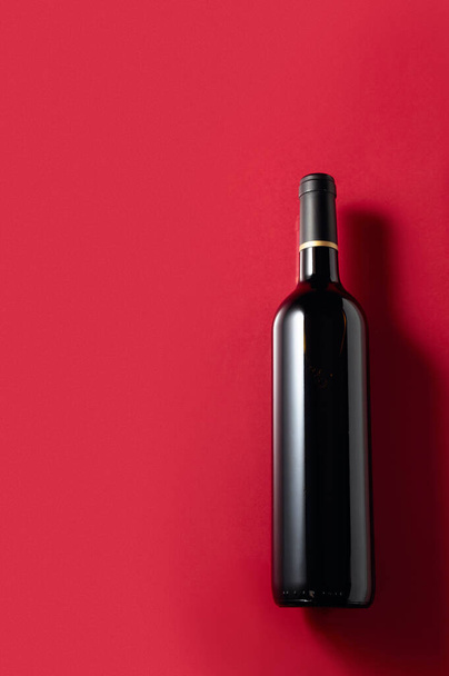 An unopened bottle of red wine on a red background. Copy space. - Photo, image