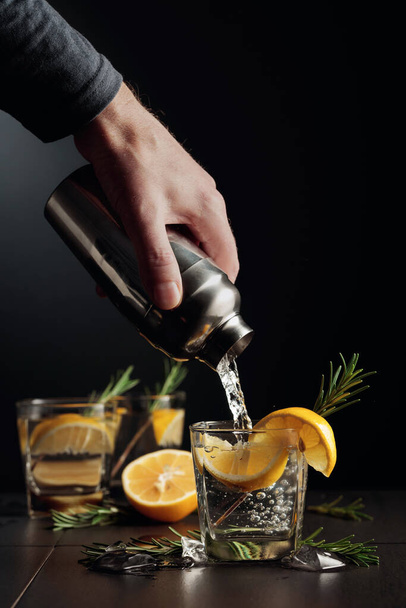 Cocktail Gin en Tonic met citroen en rozemarijn. De barman schenkt een cocktail van een shaker in een glas. - Foto, afbeelding