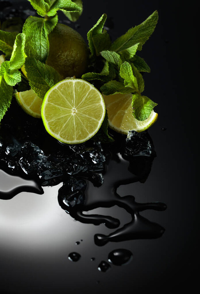 Slices of lime, mint leaves, and ice pieces on a wet black reflective background. - Photo, image