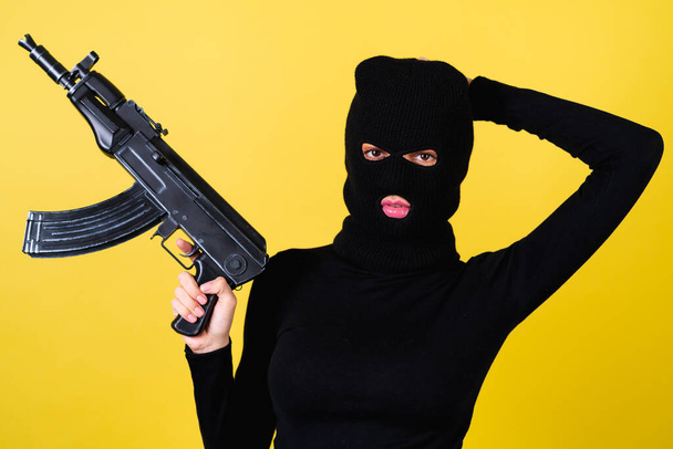 Young sexy beautiful woman with bright pink lips, balaclava on her head, holding a machine gun, bandit, thief, lawbreaker - Valokuva, kuva