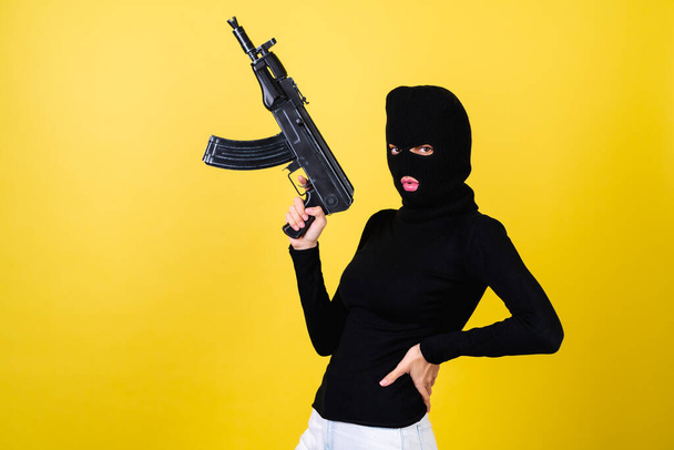 Young sexy beautiful woman with bright pink lips, balaclava on her head, holding a machine gun, bandit, thief, lawbreaker - Photo, Image