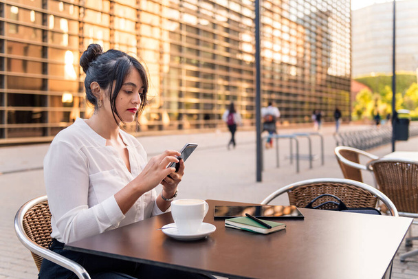 бізнес-леді консультує свій телефон на терасі кав'ярні, концепція цифрового підприємця і міського способу життя, копіювання простору для тексту
 - Фото, зображення