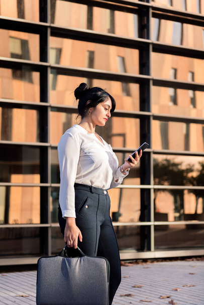 предпринимательница проверяет телефон перед офисным зданием в финансовом районе, концепцию успешного предпринимателя и городской образ жизни - Фото, изображение