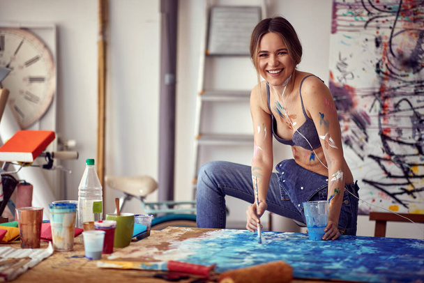 A young sexy and attractive female artist loves to pose while painting and listening to the music in a pleasant atmosphere in her studio. Art, painting, studio - Valokuva, kuva