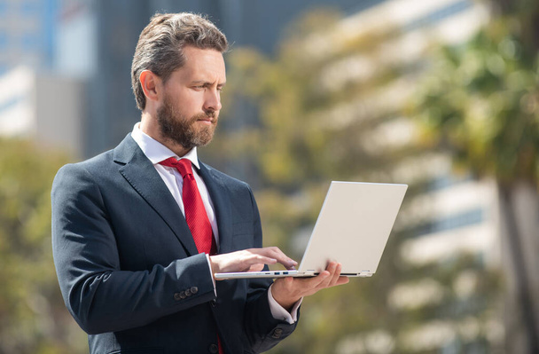 vytížený úspěšný podnikatel v obleku pracuje na notebooku stojící venku, moderní život - Fotografie, Obrázek