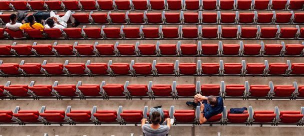 toeschouwers in het stadion in rode stoelen kijken naar de wedstrijd - Foto, afbeelding