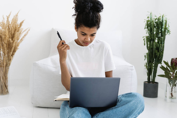 Home education, remotely work and social distancing concept. Student watch online lecture on laptop. Young concentrated african american woman doing homework, preparing new business or startup project - Foto, Bild