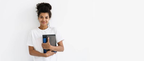 勉強、教育、広告の概念。ウェブバナーの幸せな若いアフリカ系アメリカ人女性立って本やメモ帳で手に白いコピースペースの背景に対して、笑顔、カメラを見て - 写真・画像