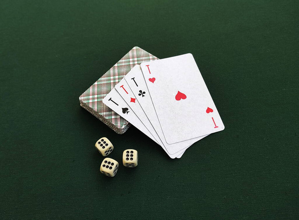 Four aces are on the deck of playing cards. Three dice with the name six are on the green table. Demonstration of gambling sports. Close-up photo. - Fotoğraf, Görsel