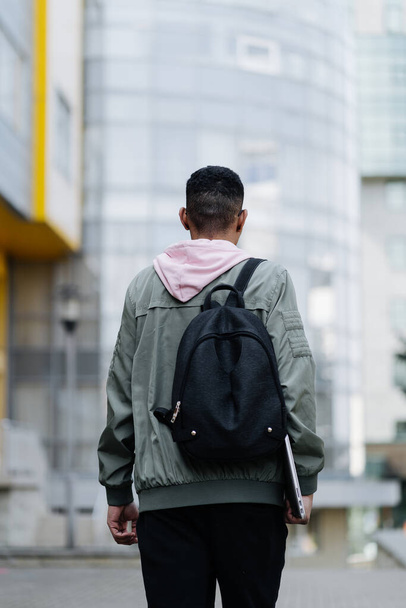Young man wearing jaket and backpack outdoors holding laptop - Foto, imagen