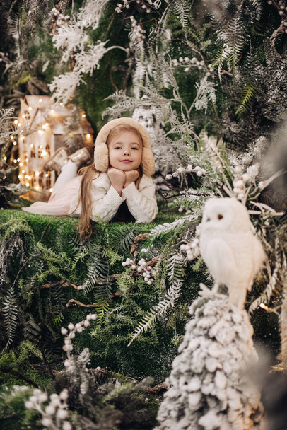 imagen de niña atractiva en ropa ligera se encuentra en una decoración de Navidad con árboles y un pequeño búho blanco - Foto, Imagen