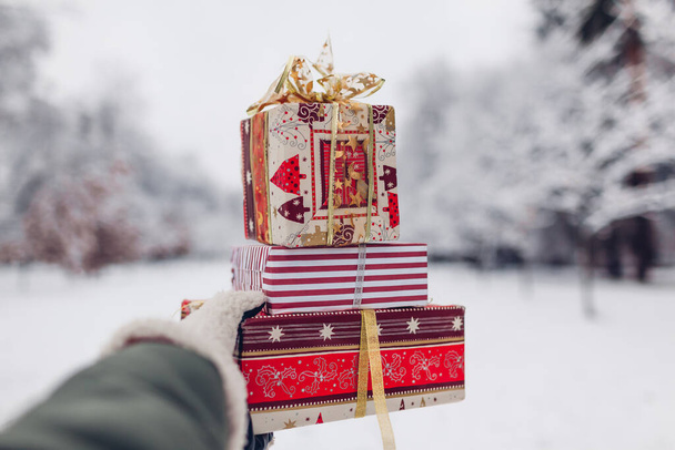 Primer plano de montón de regalos rojos de Navidad cajas de regalo en el parque de invierno nevado al aire libre en la mano femenina. Fiesta de Año Nuevo temporada de vacaciones - Foto, Imagen