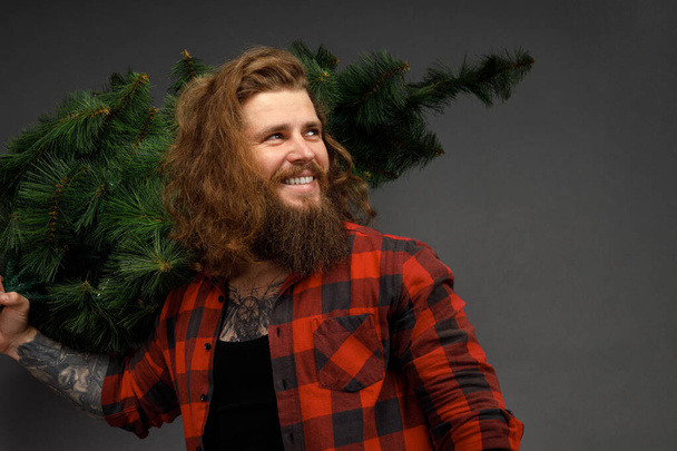 bel homme aux cheveux longs tenant un arbre de Noël synthétique. - Photo, image