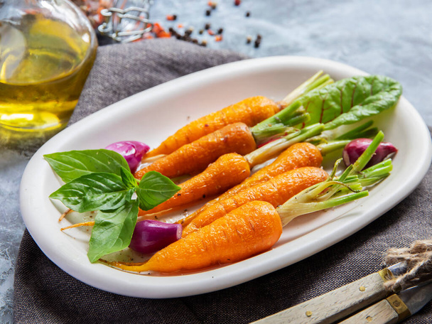 al horno de zanahorias bebé asado en un plato, albahaca y especias plato vegano de cerca - Foto, imagen