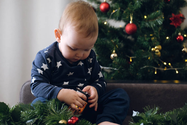 Beautiful little child on the background of a Christmas tree plays with a gift.Christmas and New Year concept - Foto, imagen