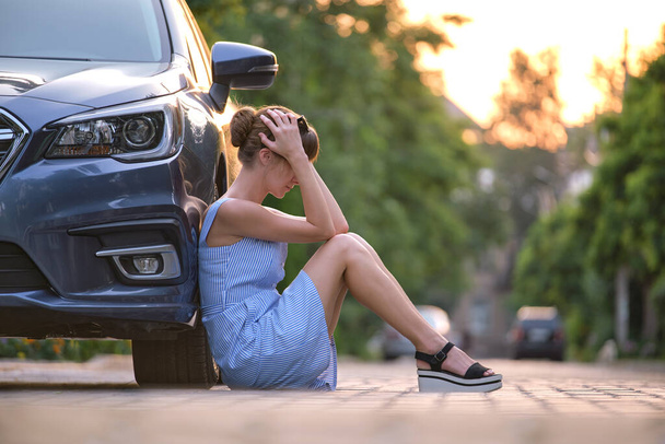 Nuori naiskuljettaja istuu rikkinäisen autonsa vieressä odottamassa apua. Ajoneuvon ongelmien käsite - Valokuva, kuva