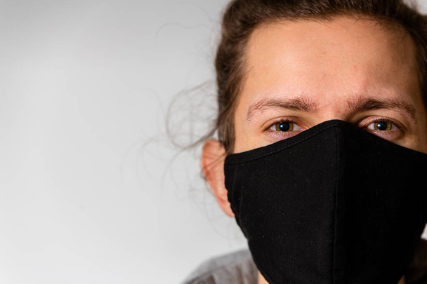 Egy fiatal férfi fekete, mosható arcmaszkot viselt a Covid-19 koronavírus világjárvány idején. - Fotó, kép