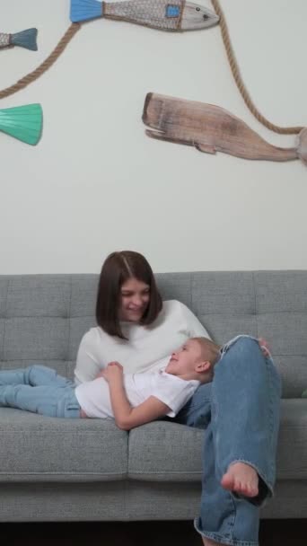 Молодая мать с маленькой блондинкой дочь сидит в комнате на диване - Кадры, видео