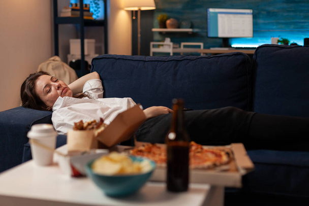 Person sleeping on sofa after drinking beer and eating home delivery pizza in front of television - 写真・画像