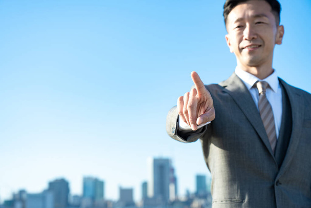A businessman posing with his index finger up on fine day - 写真・画像