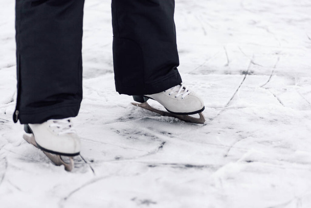 Figure skating skates. Close-up of mans legs in black winter pants standing on ice of frozen lake in white figure skating skates - Photo, image