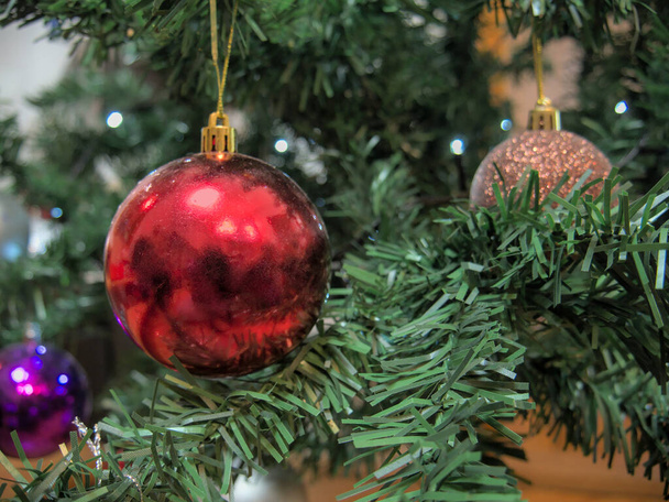 Red Christmas ball with a reflective surface, hanging on a branch of an artificial Christmas tree - Foto, afbeelding