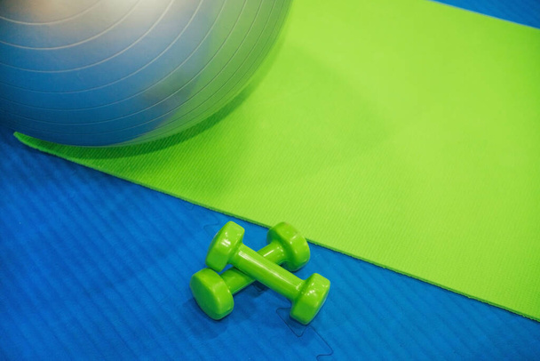 Sports equipment in the fitness center or gym. Gym ball and mat. Green dumbbells for training. The concept of a healthy and active lifestyle. - Foto, immagini