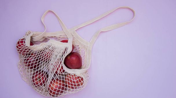 Mesh Shopping Bag. Juicy red apples are in the bag. Delicate pink background. Caring for the Environment. Healthy, organic fruits - Фото, изображение