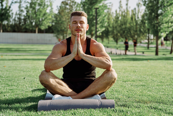 sporty man sitting on the lawn in the park training - Foto, Imagem