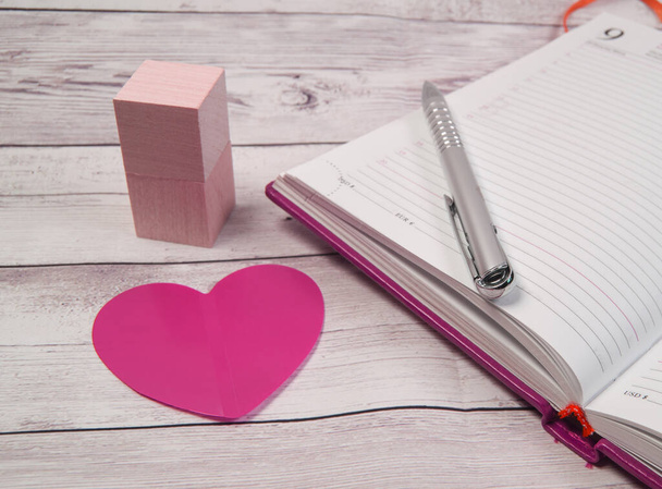 A close-up of an open diary for business reminders on Valentine's Day with a red heart and a pen. Wooden blocks on a wooden table background. - Photo, Image