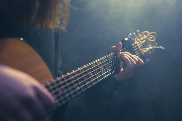 Junge Frau spielt Akustikgitarre in einem dunklen Raum mit Dunst. - Foto, Bild