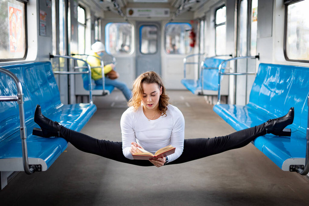 Flexible girl sitting on the split in subway and reading book. Concept of stretching and flexibility. - Fotoğraf, Görsel